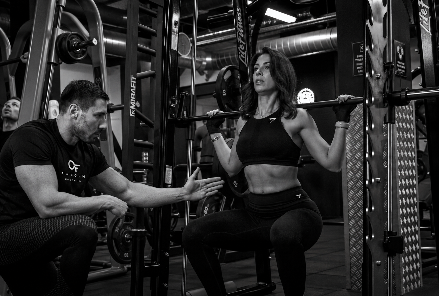 On Form LDN coach cueing a client through a barbell squat in a London gym