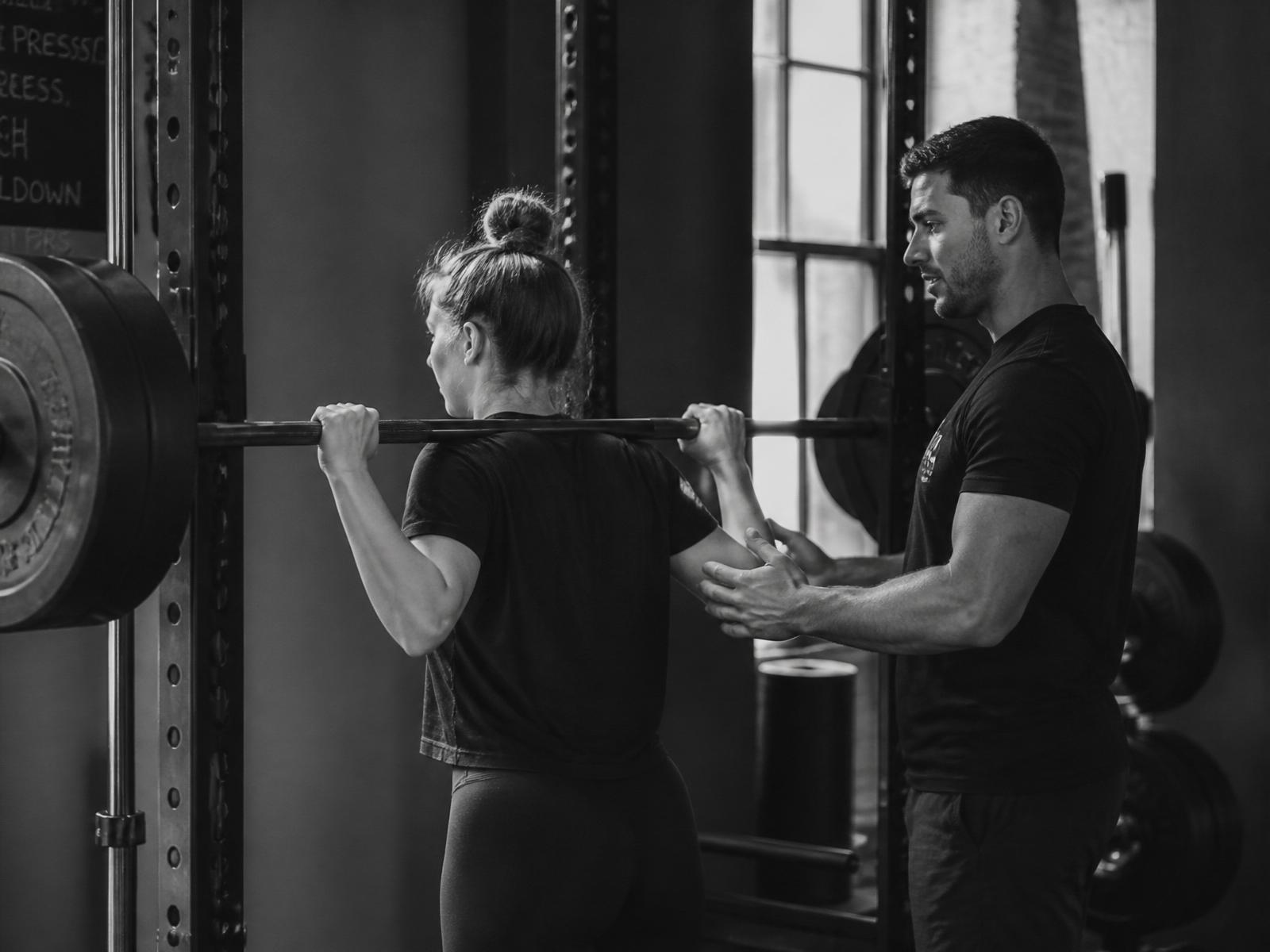 Personal trainer supporting a beginner client through a squat at the rack